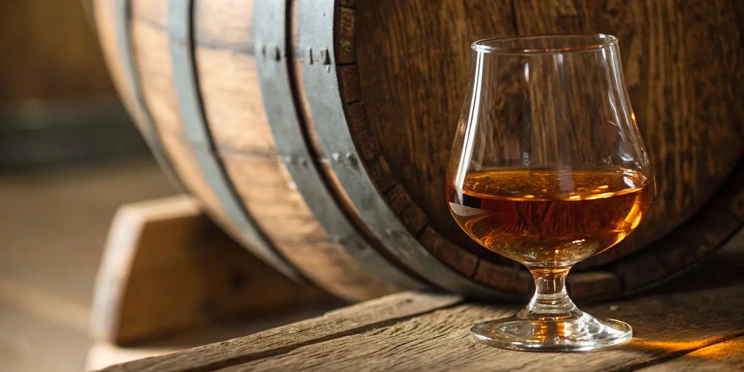 A glass of Elijah Craig bourbon resting beside a charred oak aging barrel.