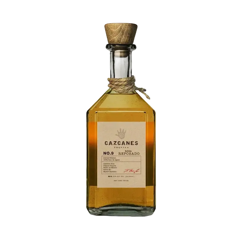 A glass bottle of Cazcanes Rosa Reposado No. 9 Tequila with a wooden stopper and a tan label detailing production information and a hand-print logo.