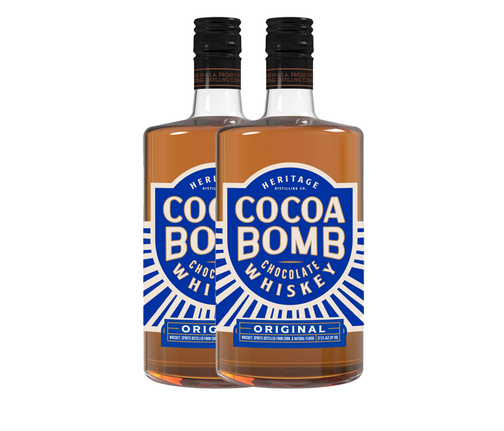 Two bottles of Cocoa Bomb Whiskey - 2 Bottle by Heritage Distilling, featuring blue and white "Cocoa Bomb Chocolate Whiskey Original" labels. The clear bottles reveal the light brown whiskey inside.