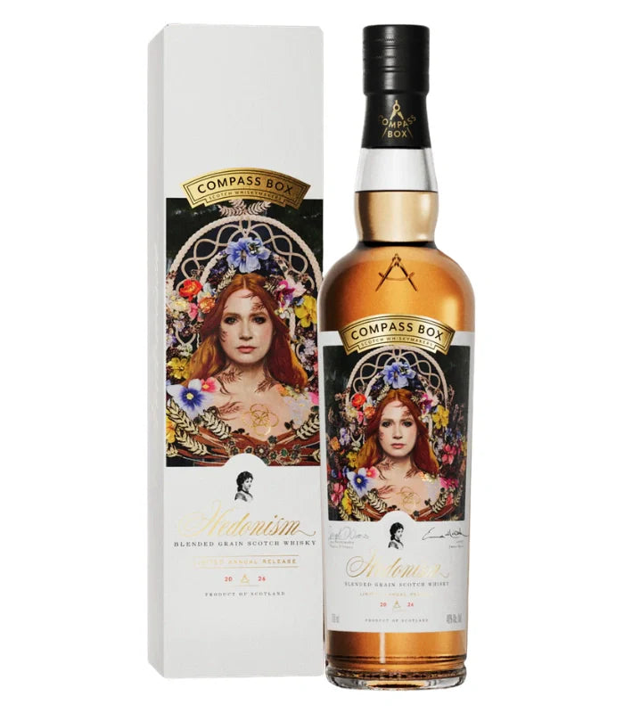 A bottle of Compass Box Hedonism 2026 Limited Annual Release Blended Grain Scotch Whisky stands beside its matching box, both adorned with an ornate label featuring a woman among colorful flowers and gold accents—an elegant annual edition.