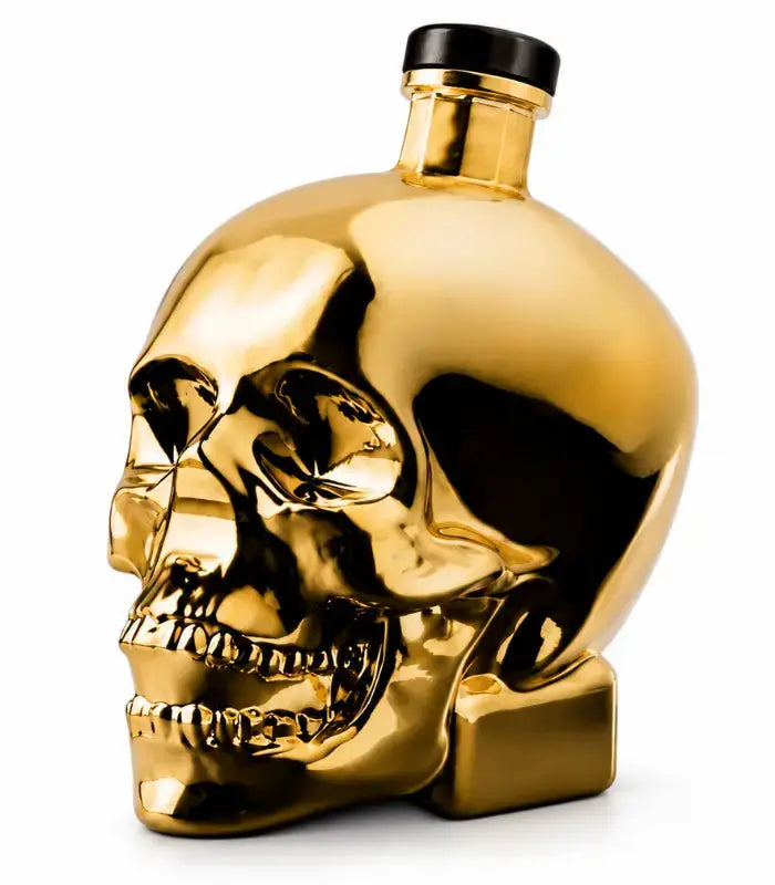 A gleaming gold Crystal Head Vodka Gold Edition (Pre-Order) bottle by Crystal Head Vodka, designed in the shape of a human skull with a black cap and set against a white background, highlights the bold and luxurious look of this premium Canadian vodka.