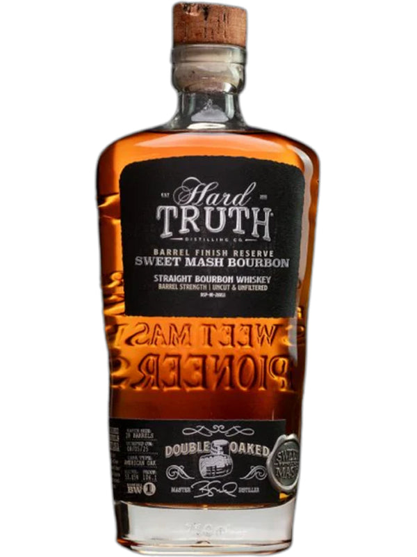 A bottle of Hard Truth Double Oaked Sweet Mash Bourbon Whiskey features a black label with white text, wooden cork, and amber liquid. "Double Oaked" and "Straight Bourbon Whiskey" are clearly printed on the label.