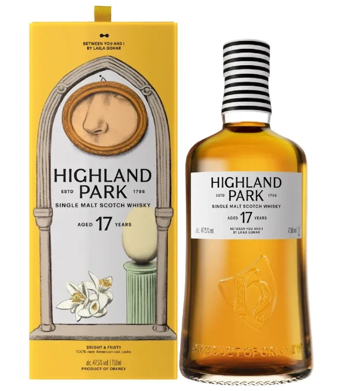 A bottle of Highland Park 17 Year Between You &amp; I Single Malt Scotch Whisky stands next to its yellow box, decorated with artistic images of a nose, flowers, and a ceramic object.