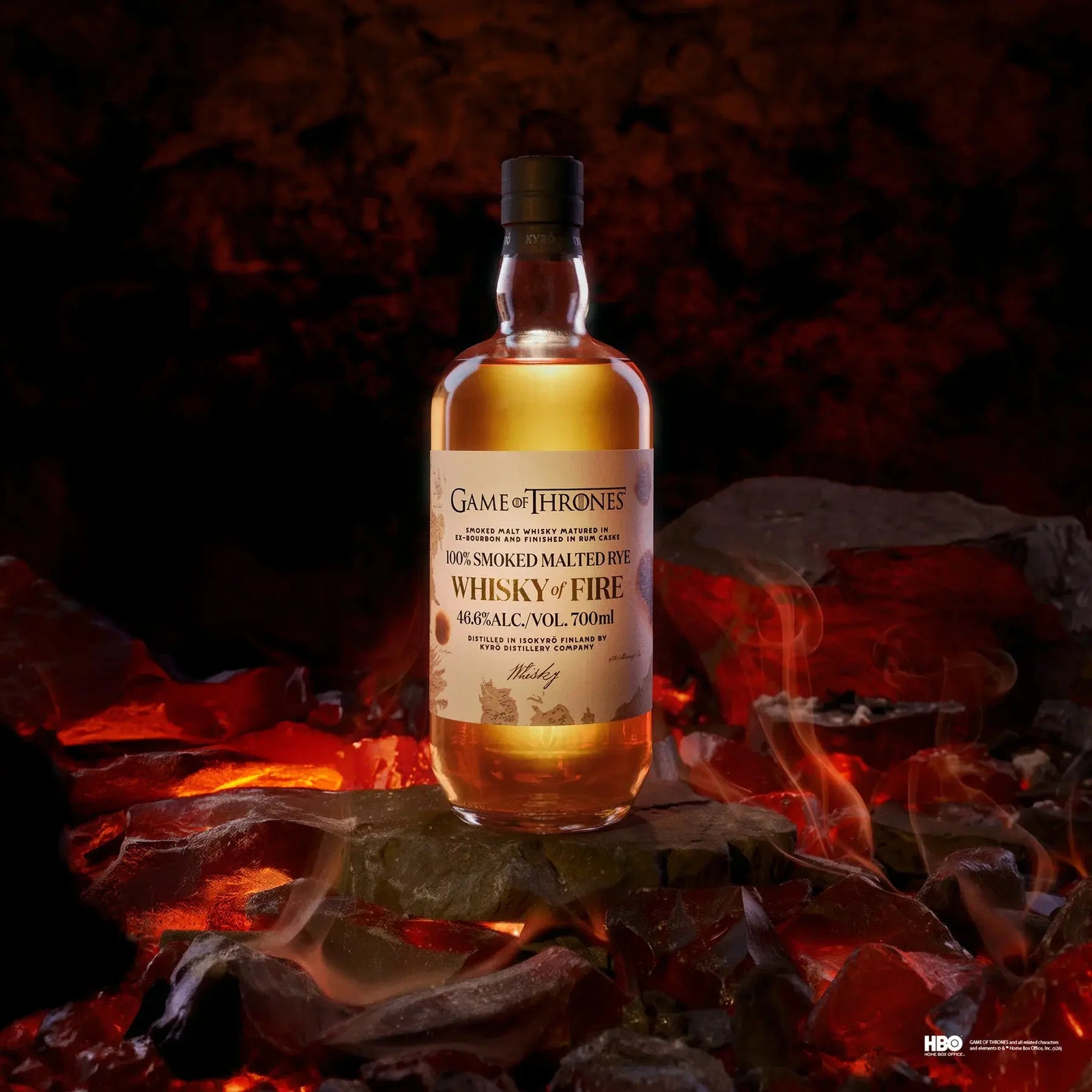 A bottle of Kyrö x Game of Thrones Whisky of Fire 700mL (PRE-ORDER) by Kyro Distillery rests on glowing embers amidst smoke and dark rocks, capturing the bold smoked malt whisky character in a fiery scene.