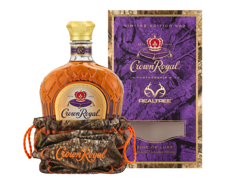 A bottle of Crown Royal x REALTREE Deluxe Limited Edition with a camo bag, shown in front of its matching purple and camouflage-patterned Crown Royal and REALTREE limited edition box.