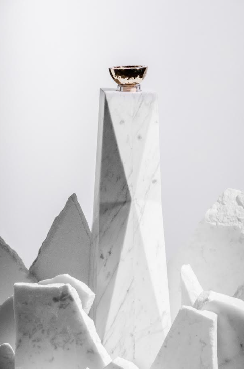 A small gold bowl atop a tall, geometric white marble pedestal with jagged marble pieces evokes the refined elegance of Volcan De Mi Tierra Coleccion I Hacienda La Gavilana Anejo Tequila, set against a plain light background.