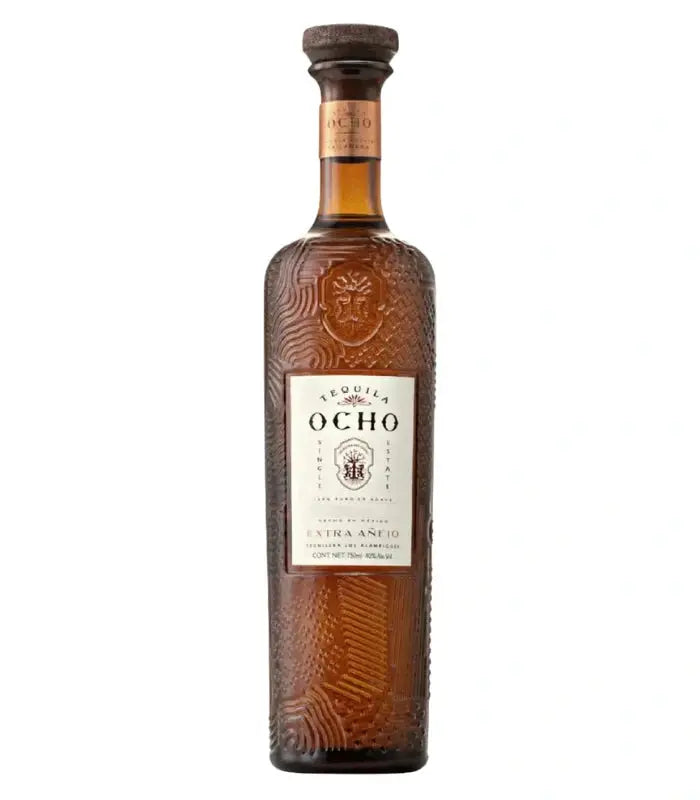 A tall, textured brown glass bottle of Ocho Tequila Extra Añejo La Cañada Estate 2022 features a cork stopper and white label with black and gold details, highlighting this luxury single estate extra añejo sipping tequila.