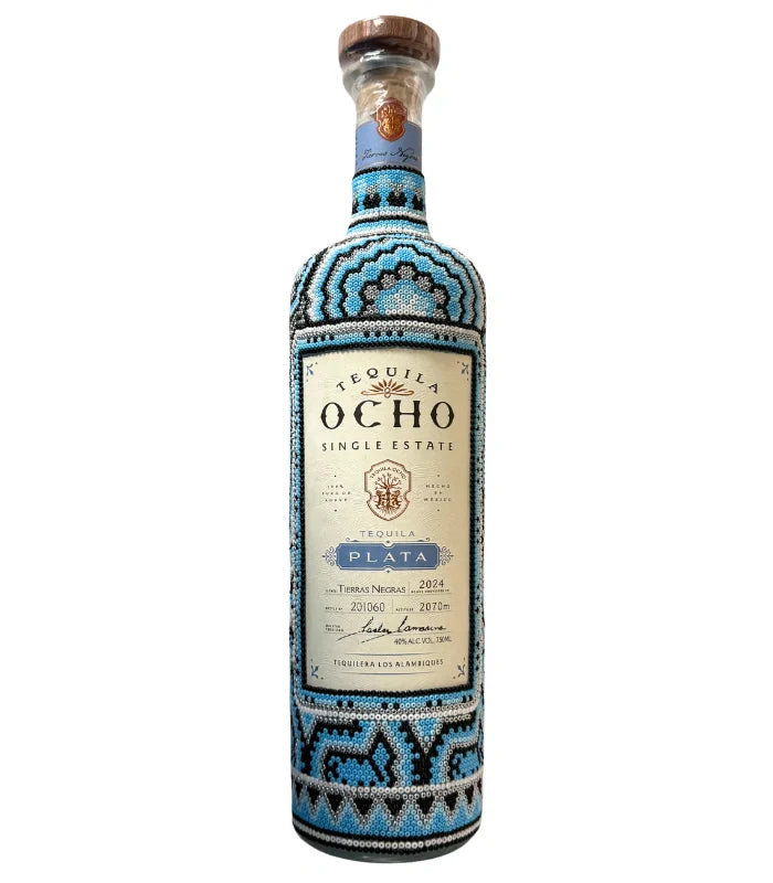 A bottle of Ocho Tequila's Tequila Ocho Plata Huichol Art Edition, featuring geometric blue, black, and white beadwork inspired by Huichol art, a wooden cap, and a detailed front label.