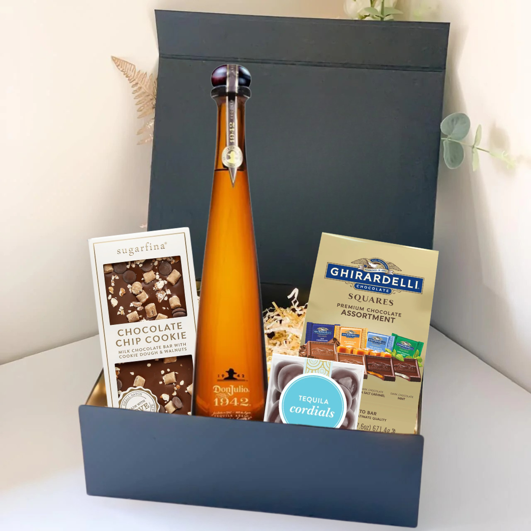 The Premium Tequila Gift Box by Main Street Liquor includes Don Julio 1942, Sugarfina chocolate chip cookie bites, Ghirardelli squares, and tequila cordials, all beautifully arranged on a white surface.