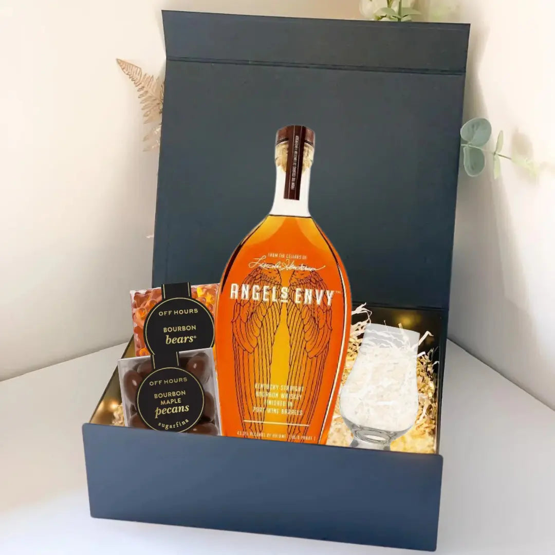 The Premium Bourbon Gift Box by Main Street Liquor includes an Angels Envy bottle, glass, filler, and two small containers labeled Off Hours Bourbon Bears and Pecans. The open box is displayed on a white surface.