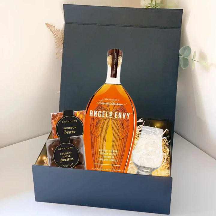 The Premium Bourbon Gift Box by Main Street Liquor includes an Angels Envy bottle, glass, filler, and two small containers labeled Off Hours Bourbon Bears and Pecans. The open box is displayed on a white surface.