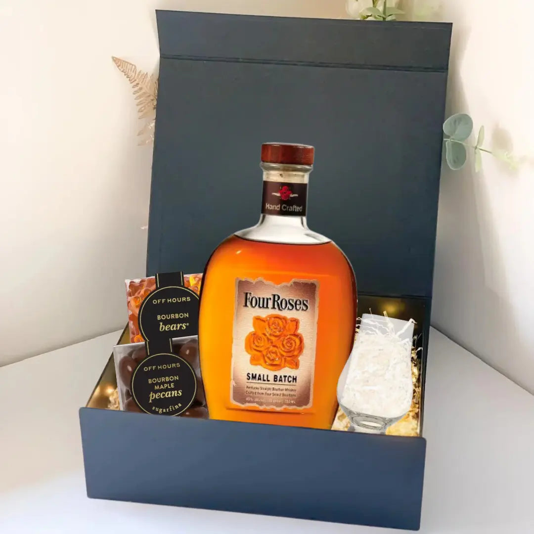 The Premium Bourbon Gift Box by Main Street Liquor includes a Four Roses Small Batch bottle, two small jars of bourbon pecans and bourbon bears, a clear glass, and decorative string lights—all in an elegant black box.