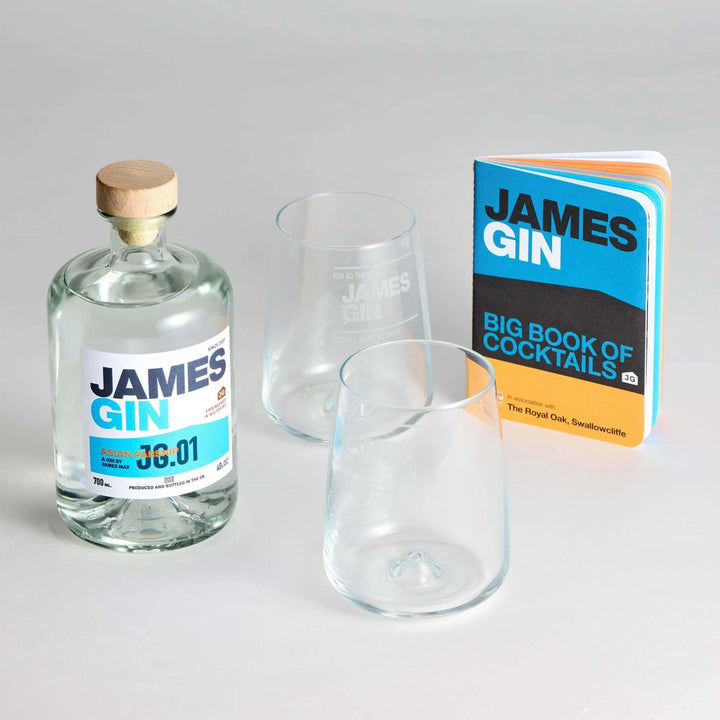 The James Gin US The Mixologist's Cocktail Kit with a Souvenir Gift Key Chain, featuring two clear glasses and a vibrant cocktail book, is displayed on a light gray surface.